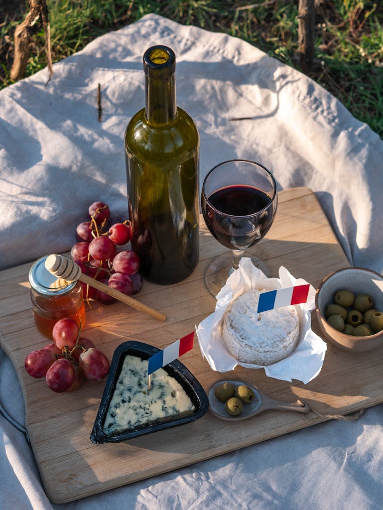 A charming French picnic with wine, cheese, and fruits on a wooden board outdoors.