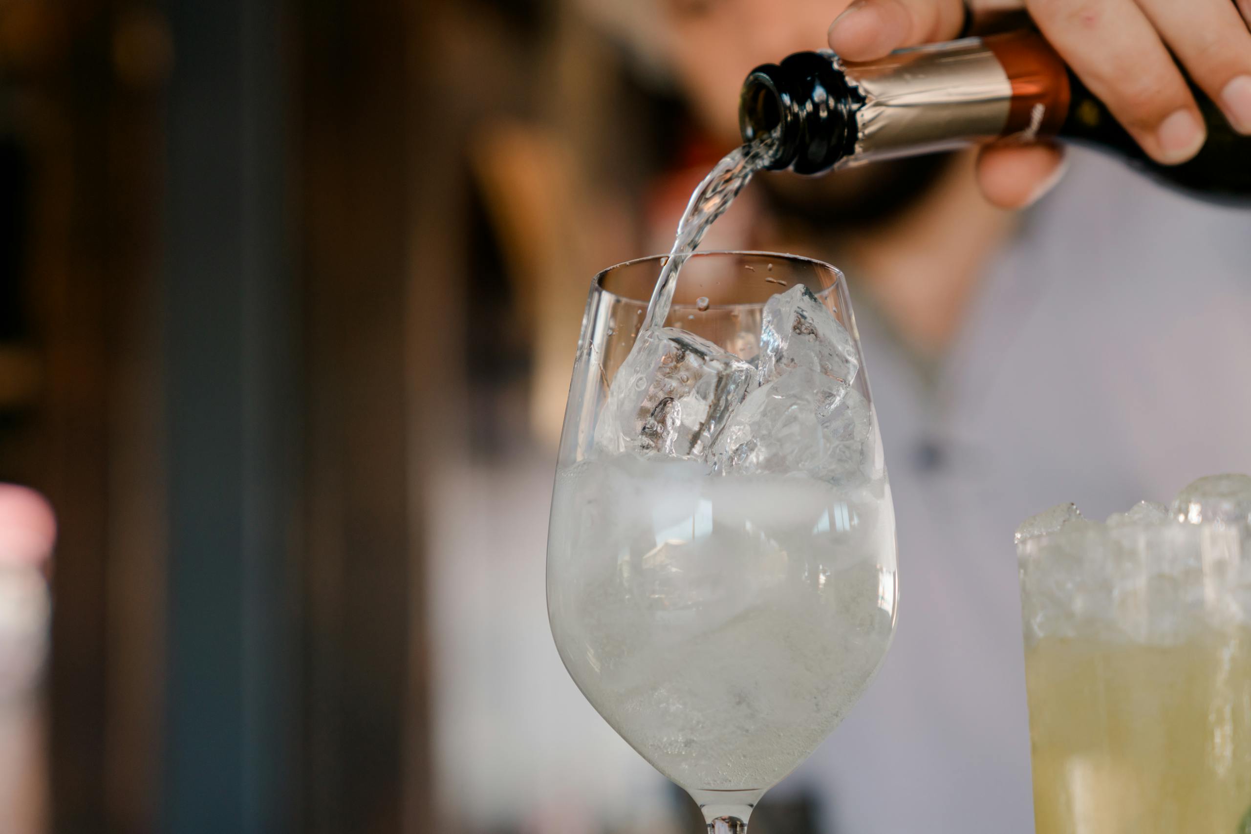 A sparkling beverage being poured into a wine glass filled with ice cubes, creating a refreshing summer drink.