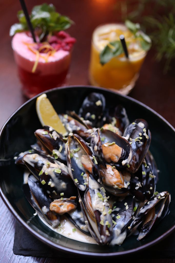 Delicious mussels in creamy sauce with colorful cocktails in a cozy setting.